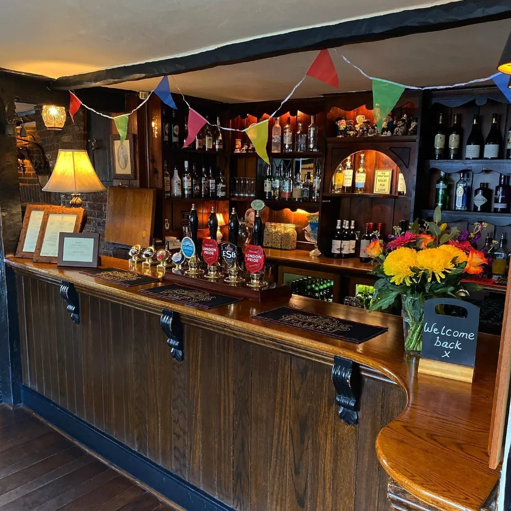 The Holly Bush bar: dark polished wood, hand pumps for London Pride, ESB and Seafarers, bunting along the beam and a vase of flowers on the counter.